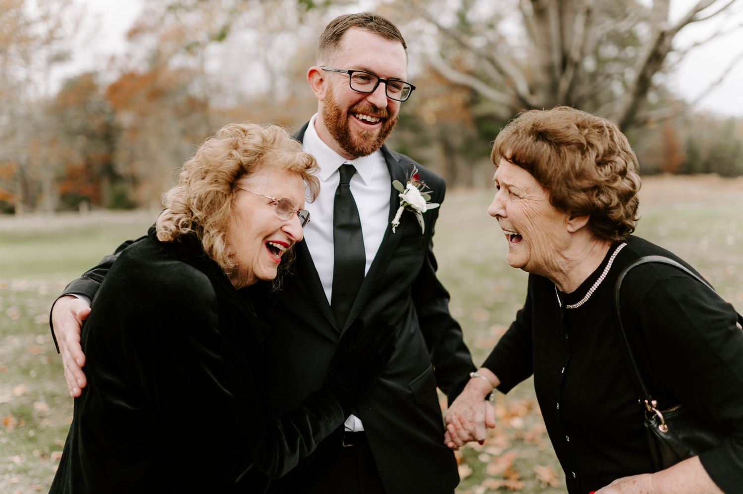 Three people share a candid laughing moment at an outdoor wedding celebration.
