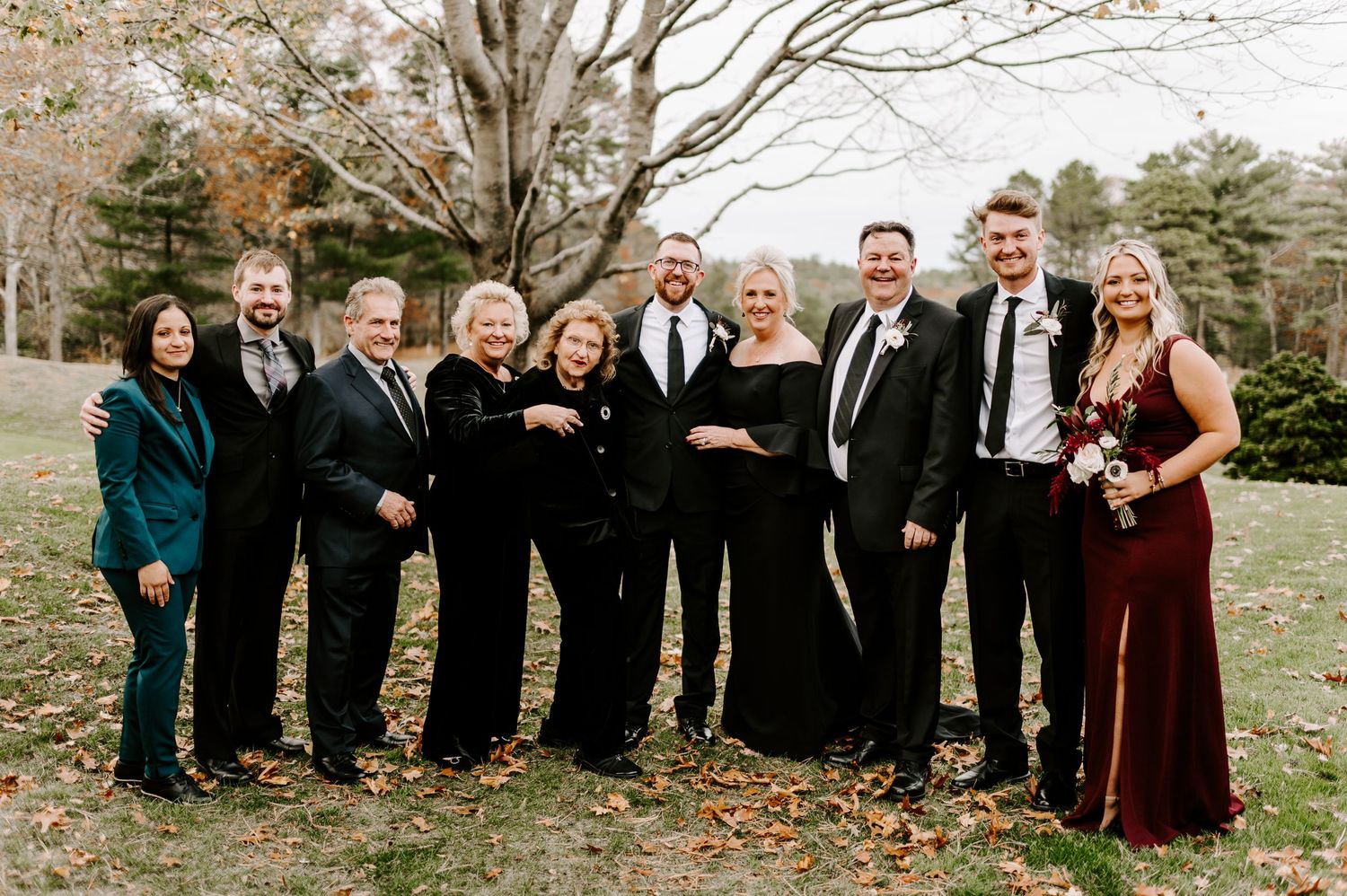 Large family group photo with wedding party members in formal black attire outdoors.