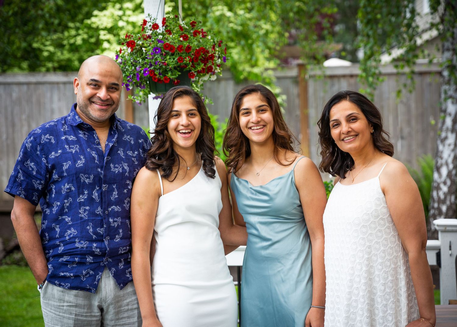 A family group in summer attire poses together in a backyard garden with blooming flowers.