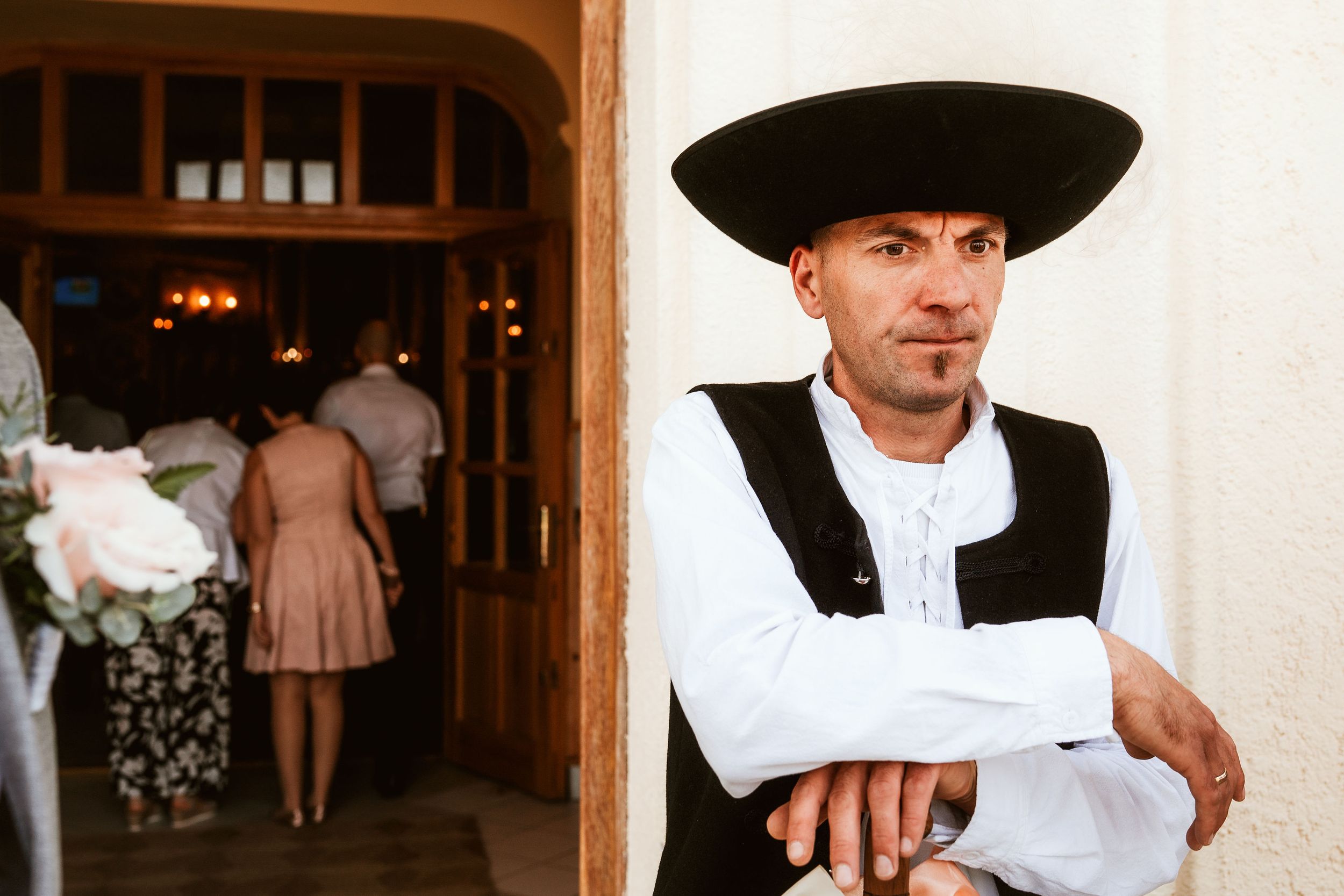 A person in traditional black and white attire leans against a wall near an archway.
