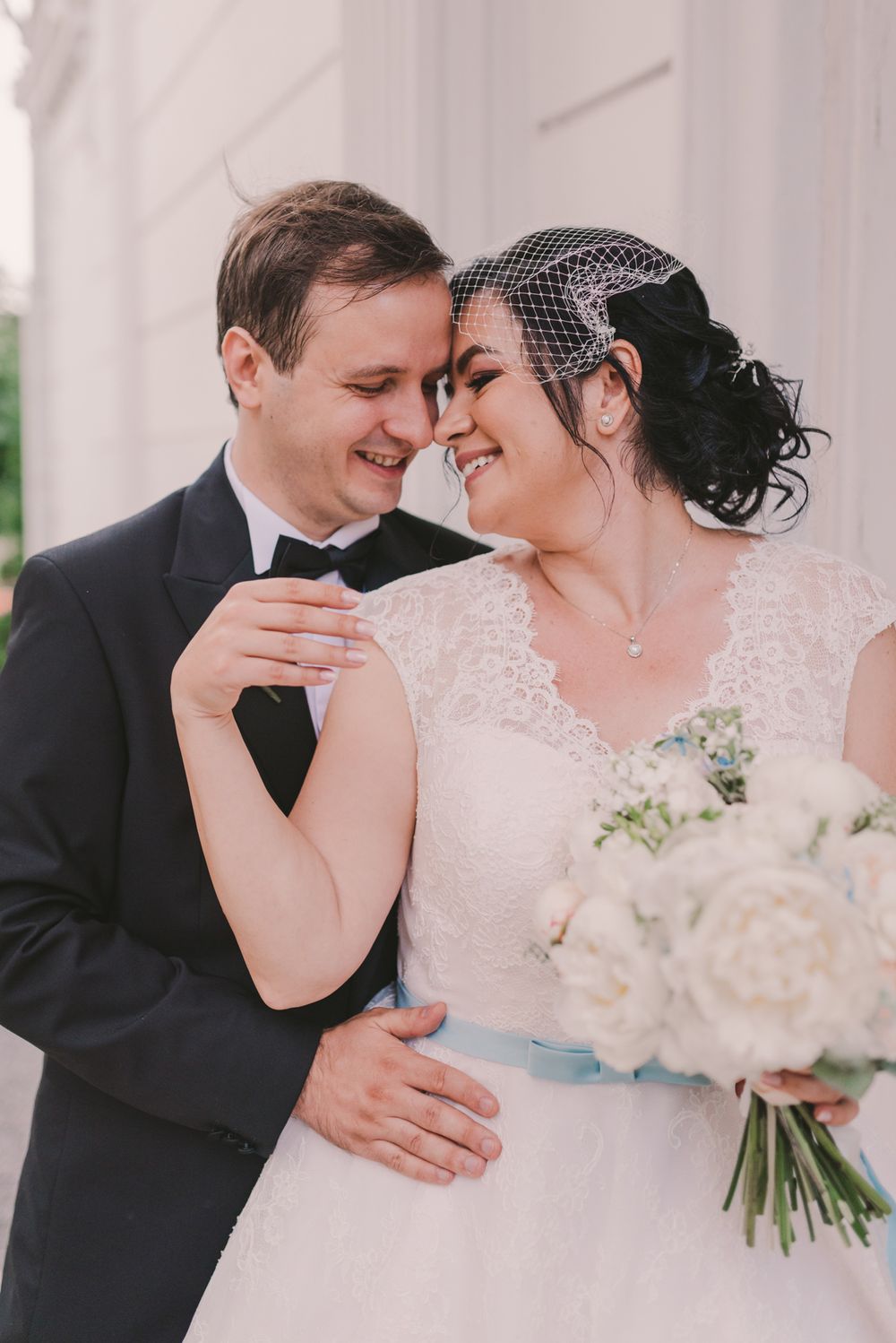 Tender wedding moment captured against white pillars with a beautiful floral bouquet.