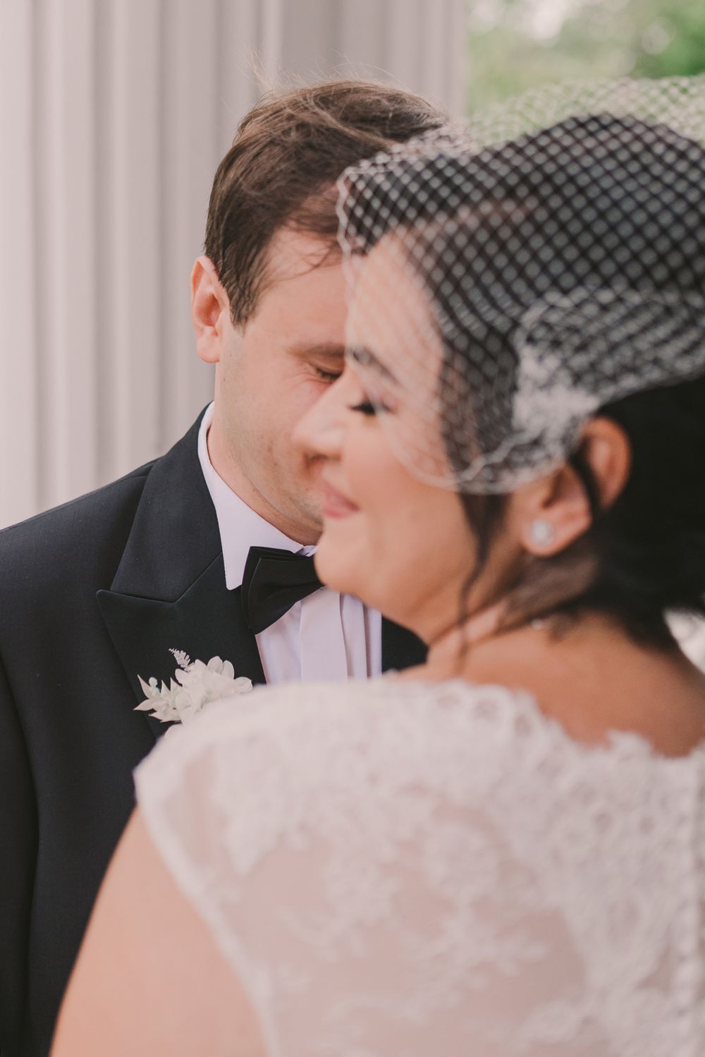 Romantic close-up of newlyweds sharing a tender moment by white columns.