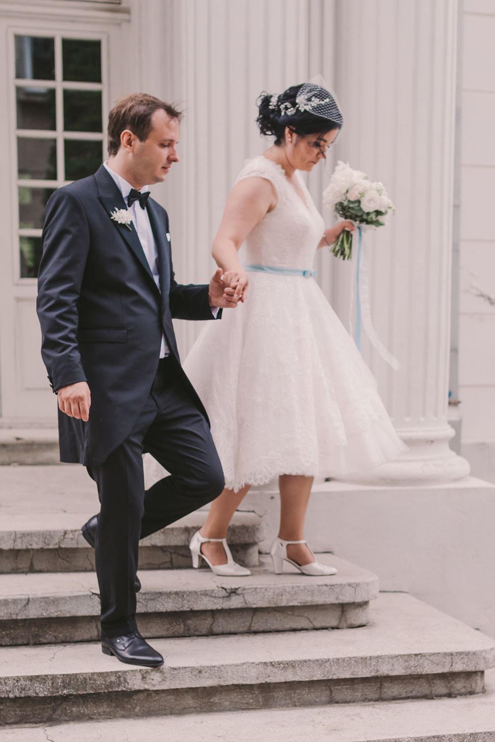 Wedding couple ascending stone steps outside a classical building with white columns.