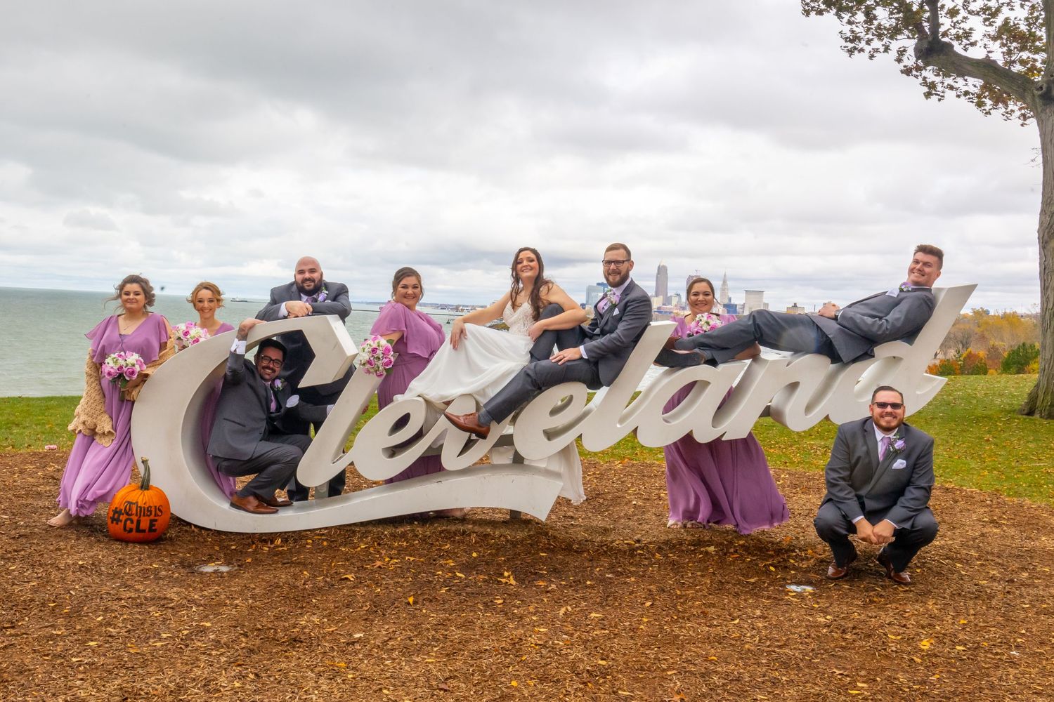 Wedding party poses playfully on large Cleveland sign with lake view in background.