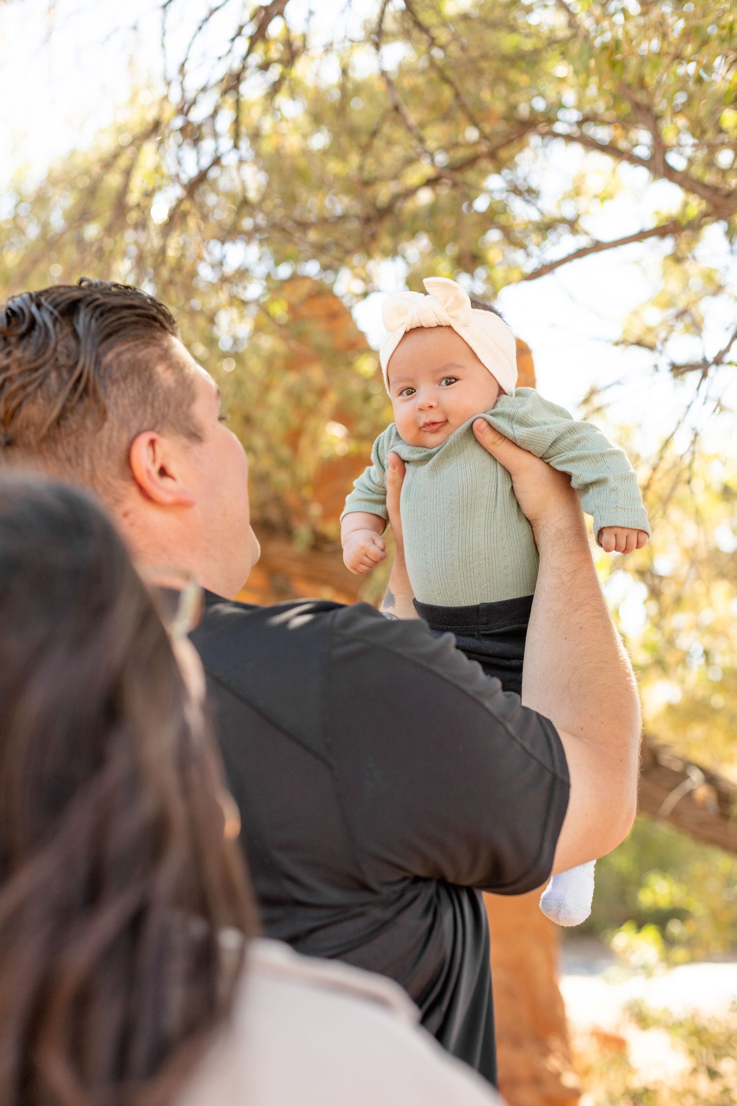 Parents holding up a baby wearing a light colored outfit during an autumn photoshoot.