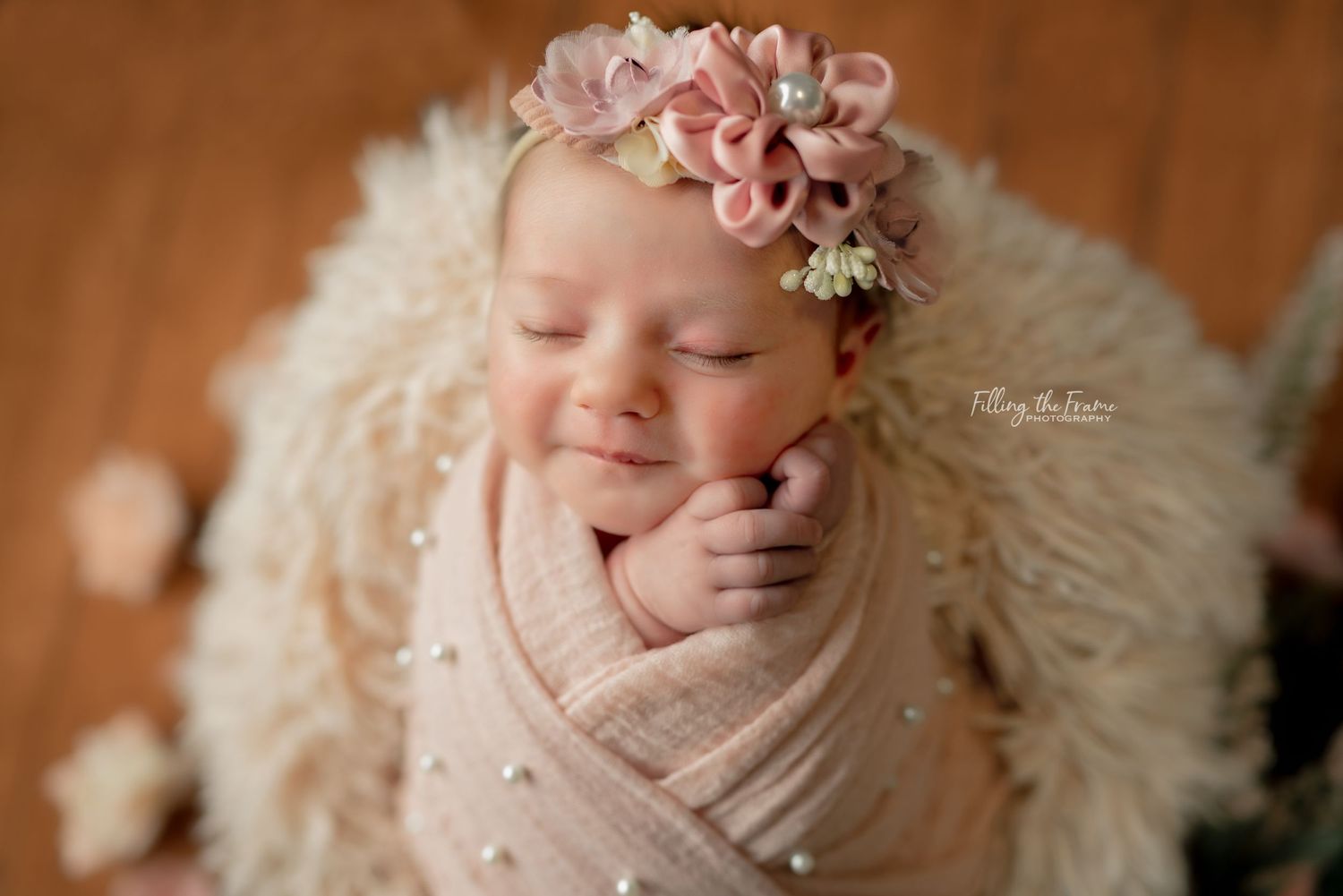 Delicate newborn portrait with pink floral accents and white feather wrap.