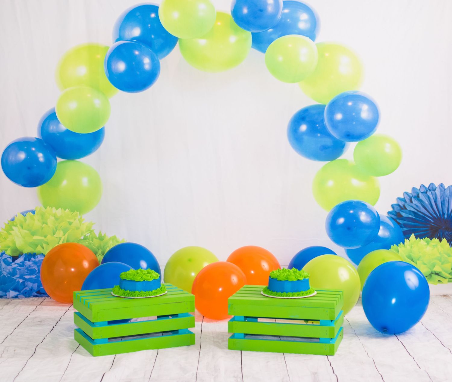 Green platforms arranged under blue and lime balloon arch for photography setup.