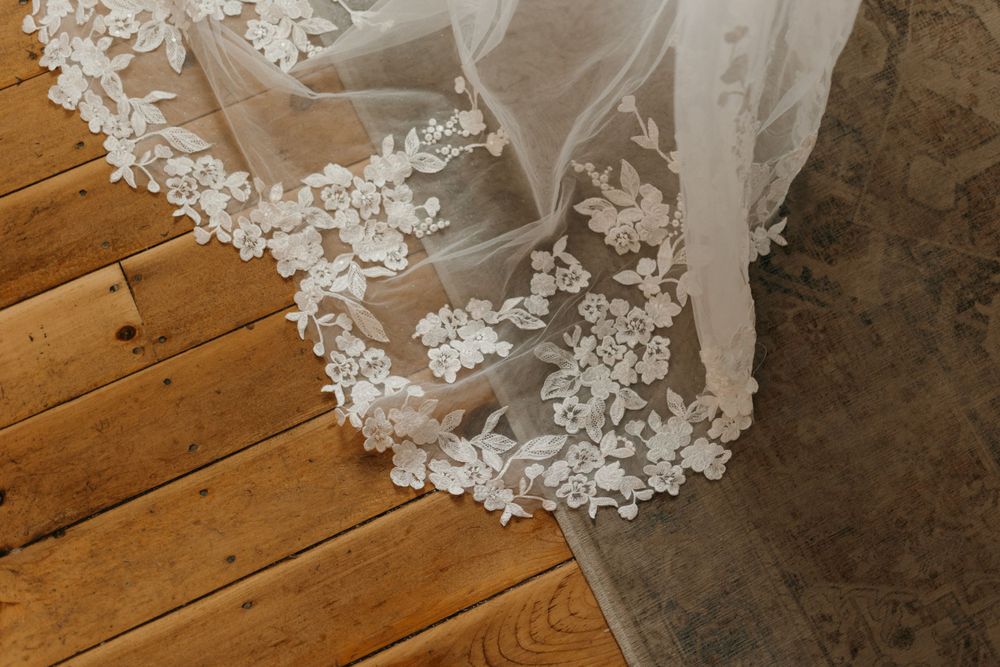 Intricate floral lace detail of a bridal veil spreads gracefully across warm hardwood floors.