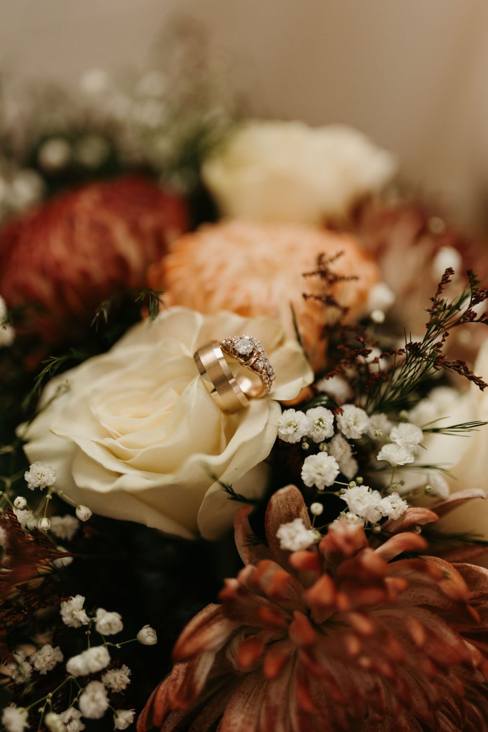 Wedding rings resting on white rose in bridal bouquet with proteas and baby's breath flowers.