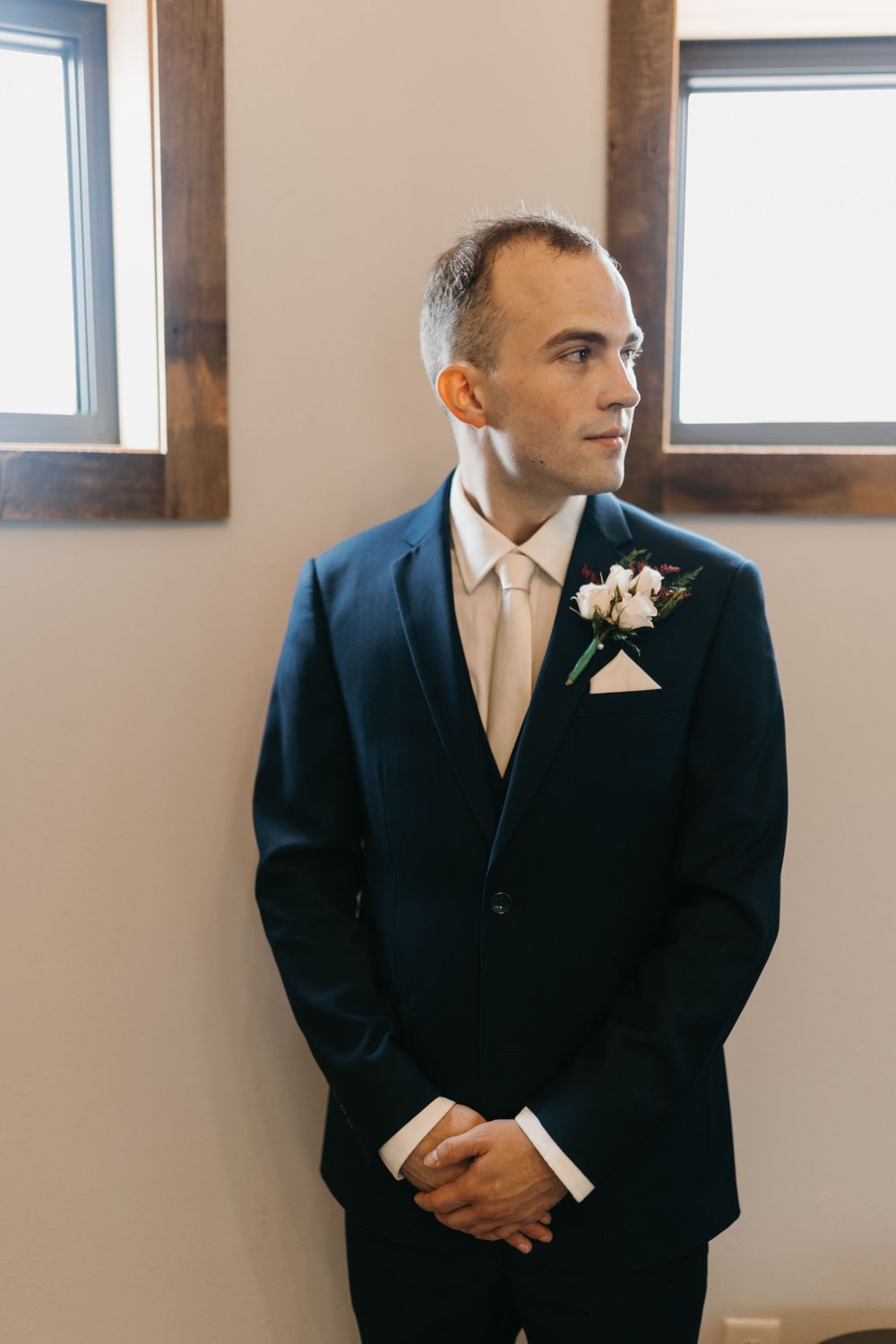 Groom in navy suit with cream tie and boutonniere gazing thoughtfully to the side.