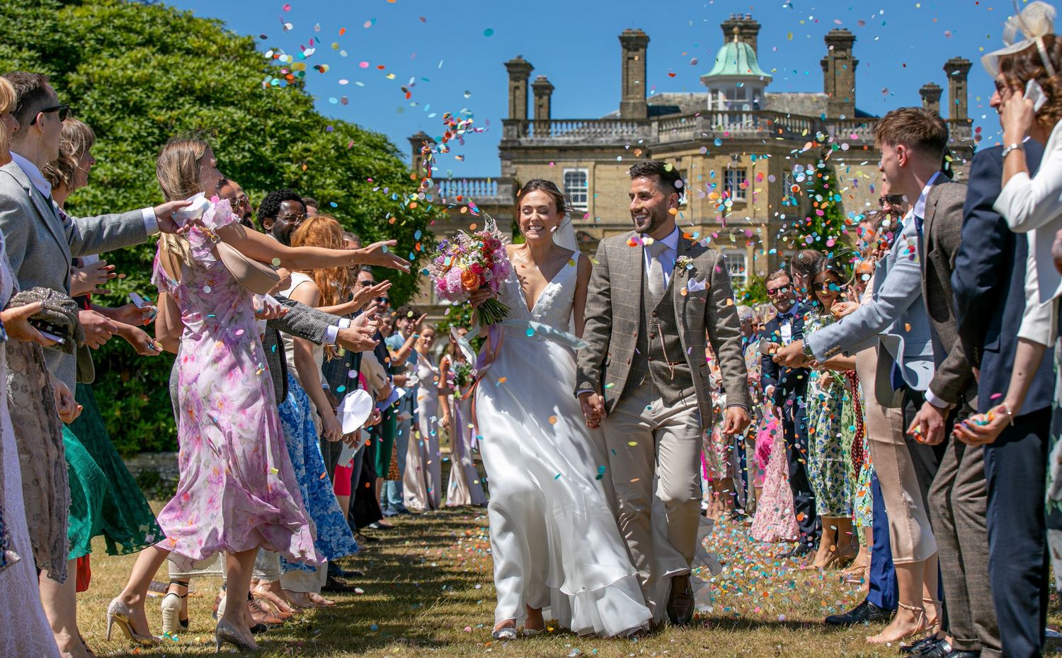 Wedding guests tossing confetti over the couple on the grounds of a historic building.