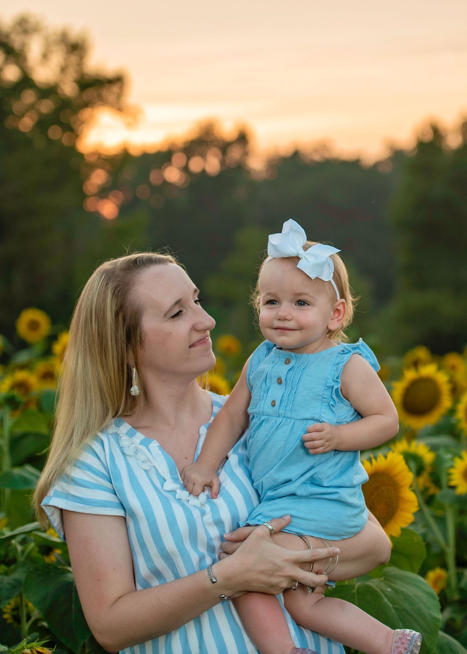 Mother and child among blooming sunflowers at sunset.