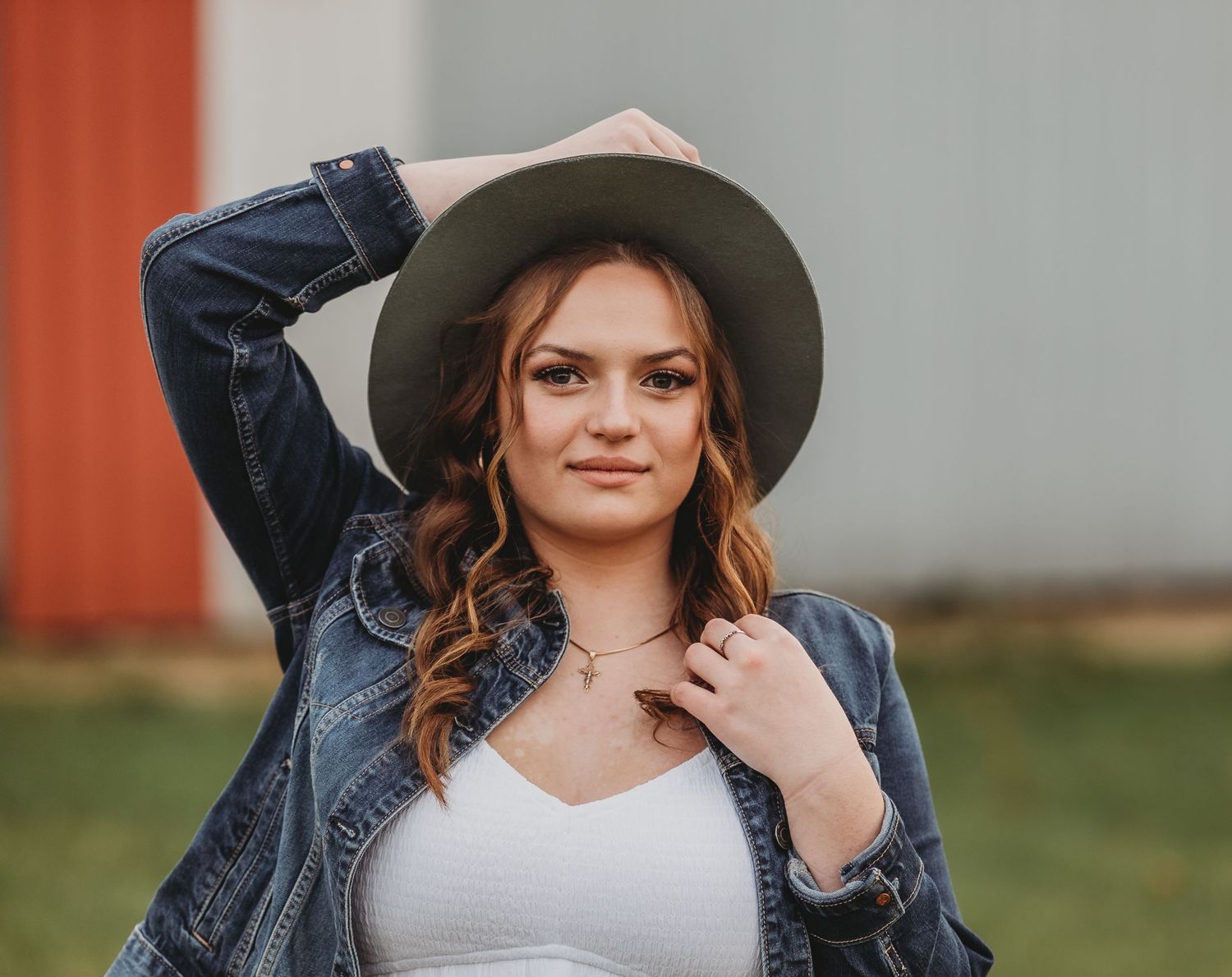 A casual outdoor portrait featuring a denim jacket, grey hat and wavy hair styled with natural lighting.