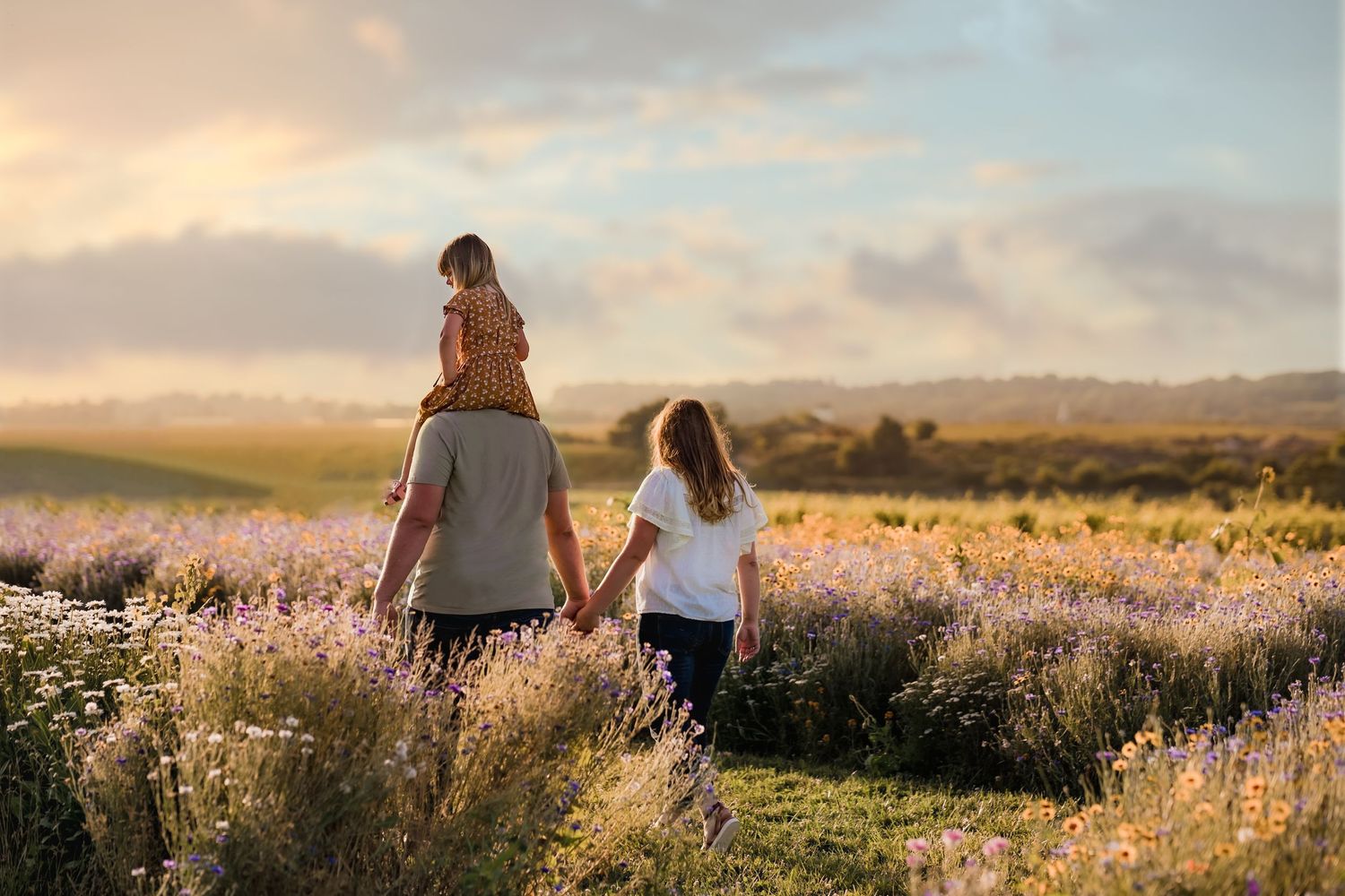 People walking through scenic wildflower meadow with mountains in background at sunset.