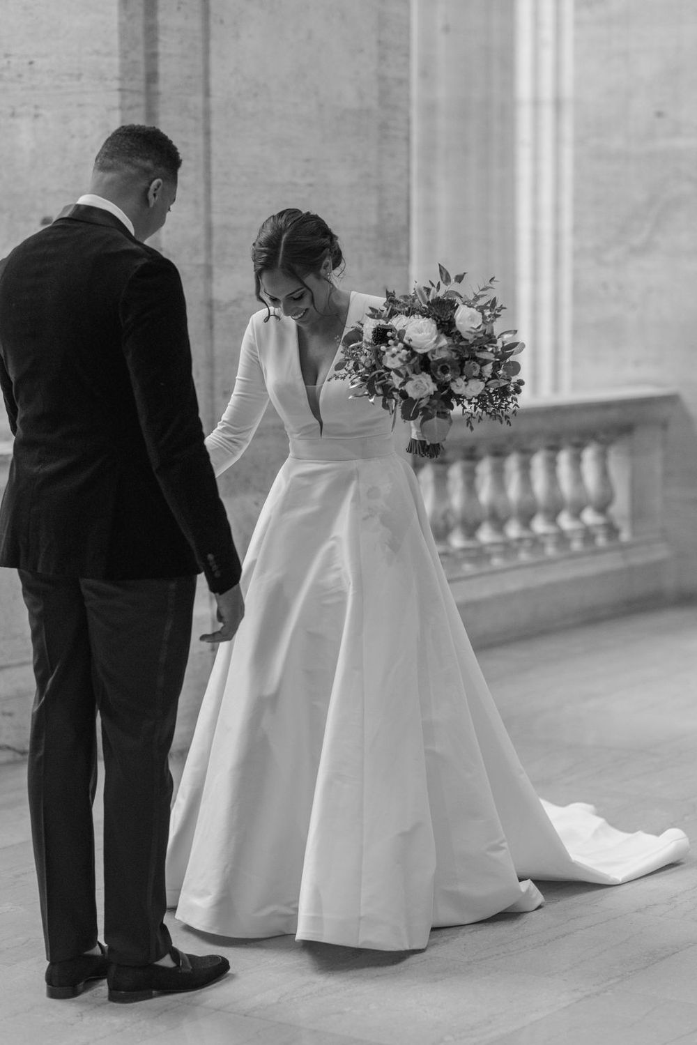 Black and white photo of wedding couple sharing intimate moment in grand hallway.