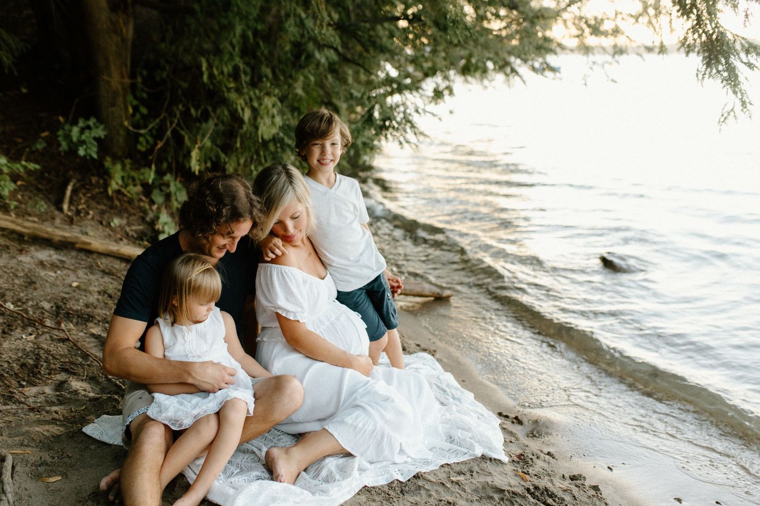 A family sitting together on a white blanket at the beach during sunset while water laps at the shore.