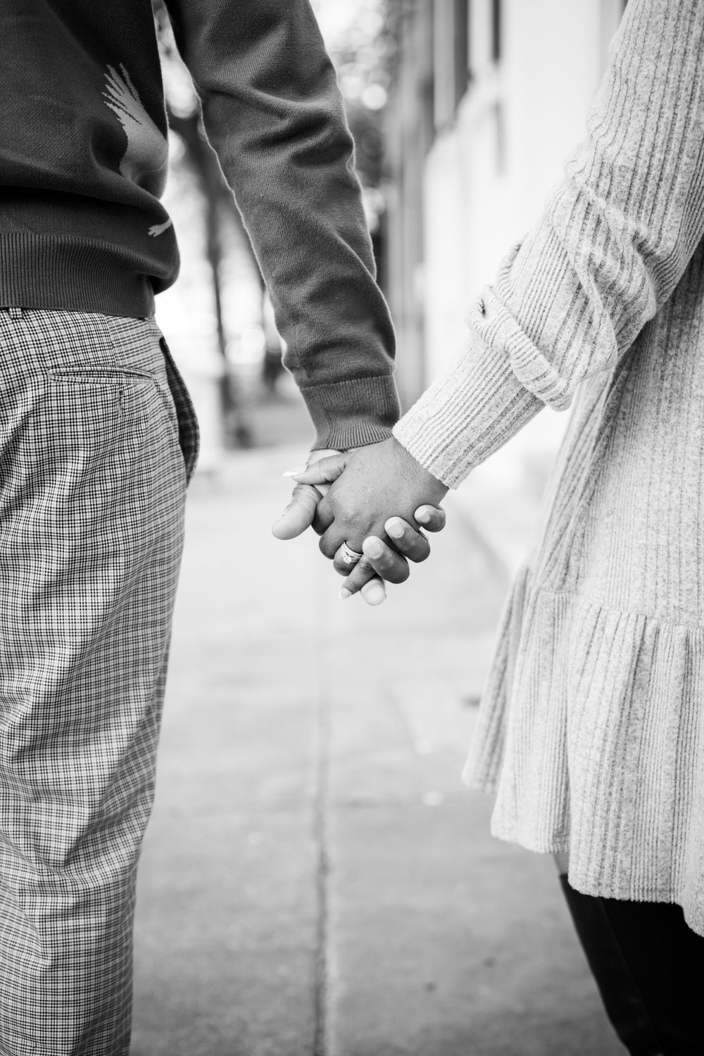 A close-up black and white photo of a couple holding hands while standing together.