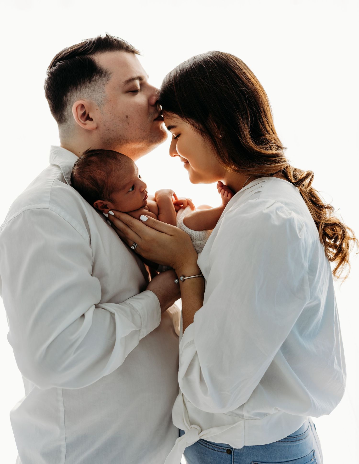 Intimate family portrait with parents in white shirts sharing tender moment with newborn baby between them.
Rashinphotography-Nova DC DMV