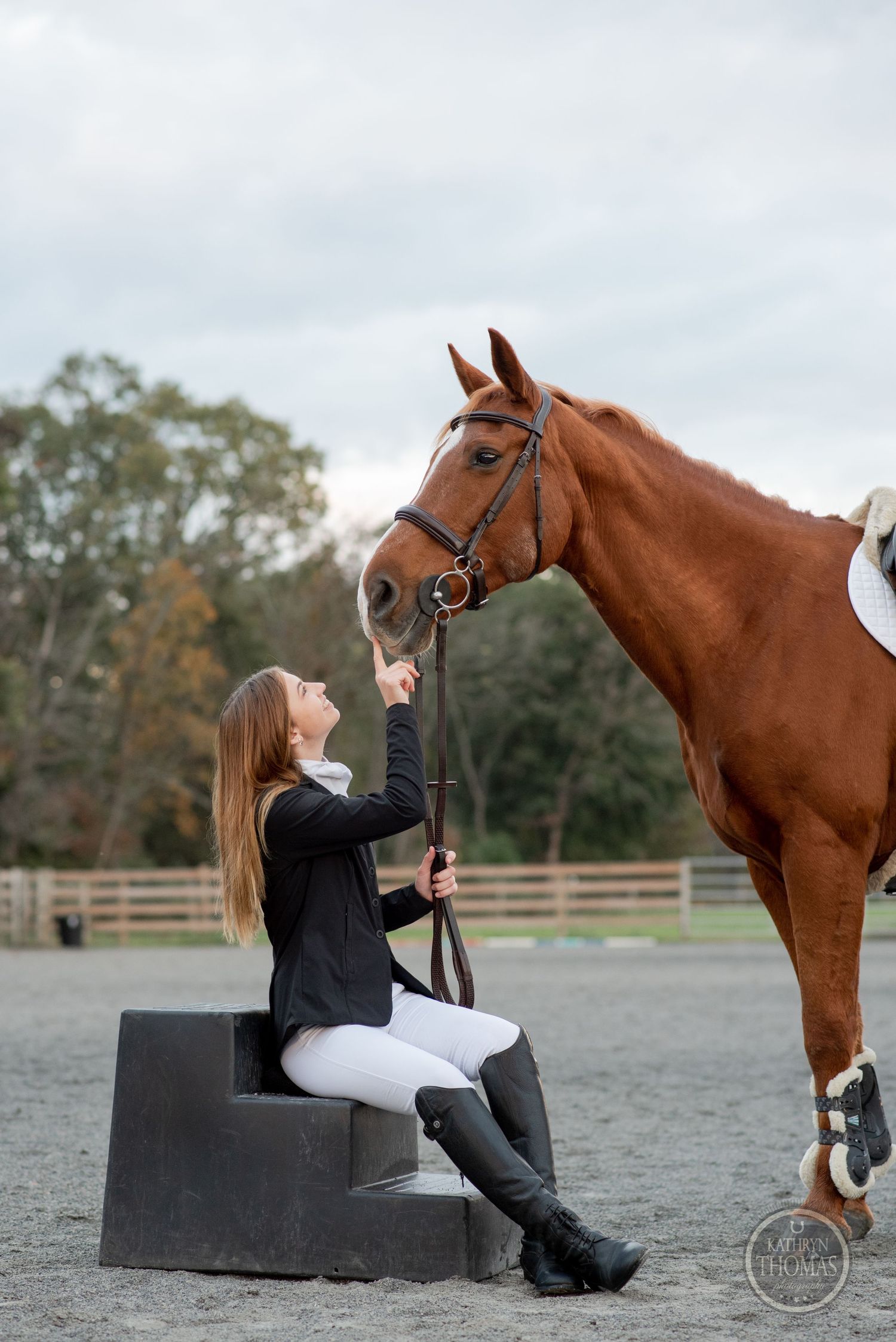 Equestrian and horse sharing moment while sitting on mounting block in arena.