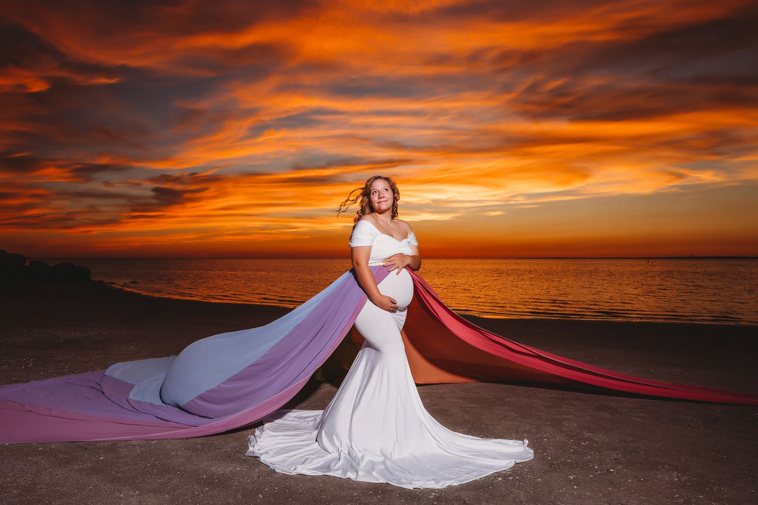 Sunset beach portrait with flowing red and pink fabric against orange sky.