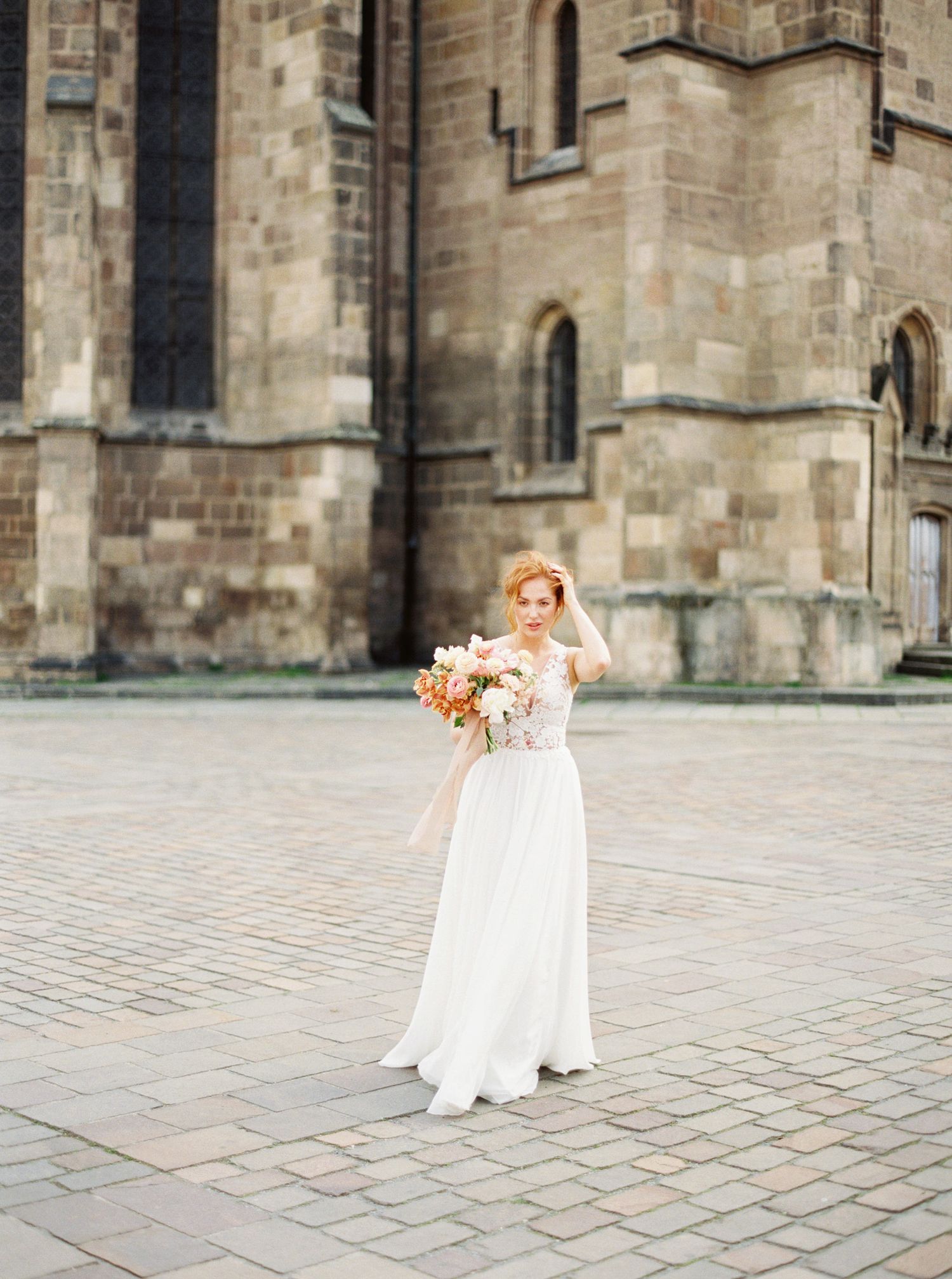 A bride in a white dress standing in front of a church in Prague.