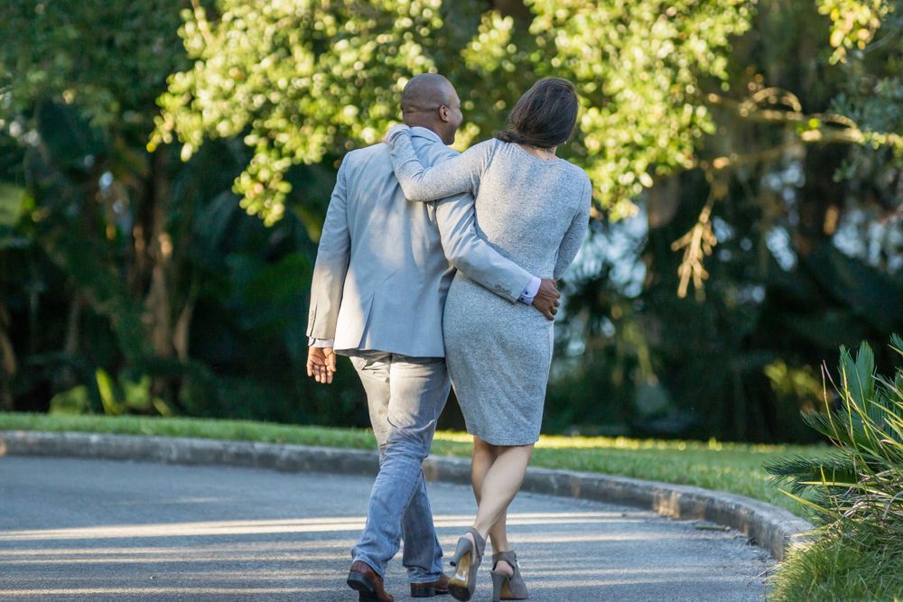 A couple walking arm in arm down a curved garden path on a sunny day.