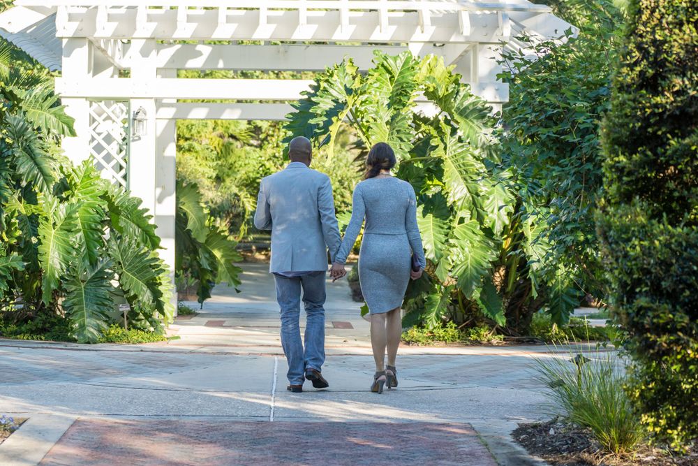 Couple walking together on garden path under white pergola.