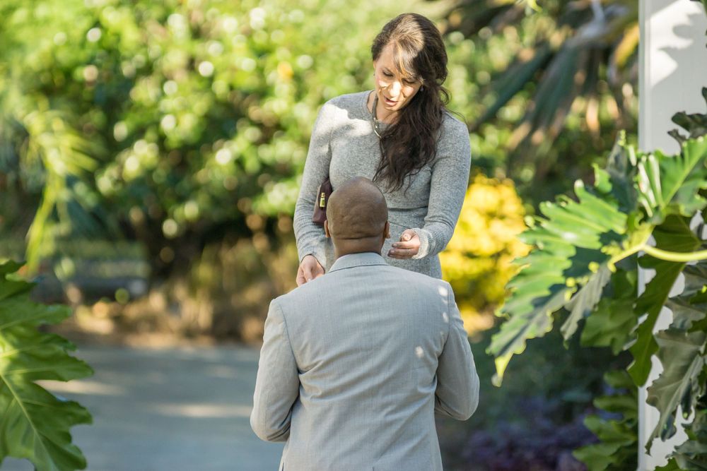 A couple shares a tender moment in a lush garden path during a marriage proposal.