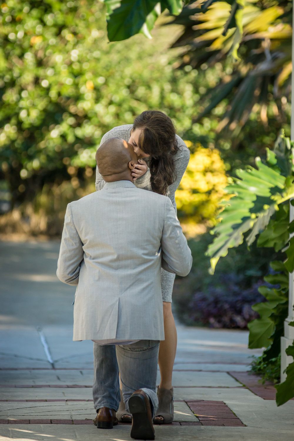 A romantic proposal moment captured in a sunlit garden pathway.