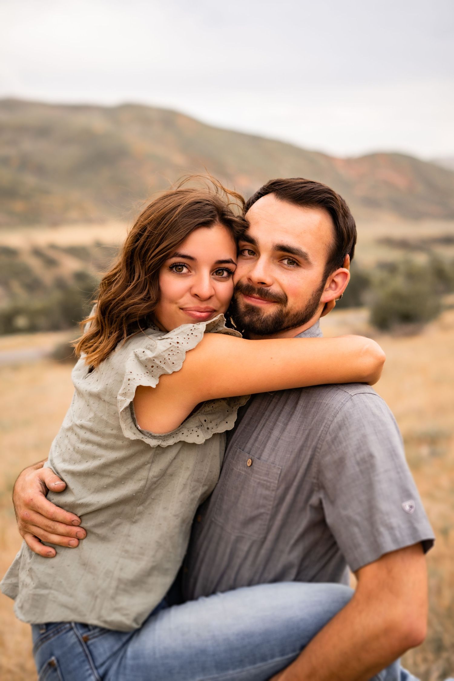 Romantic couple embracing in an outdoor setting with mountains in the background.