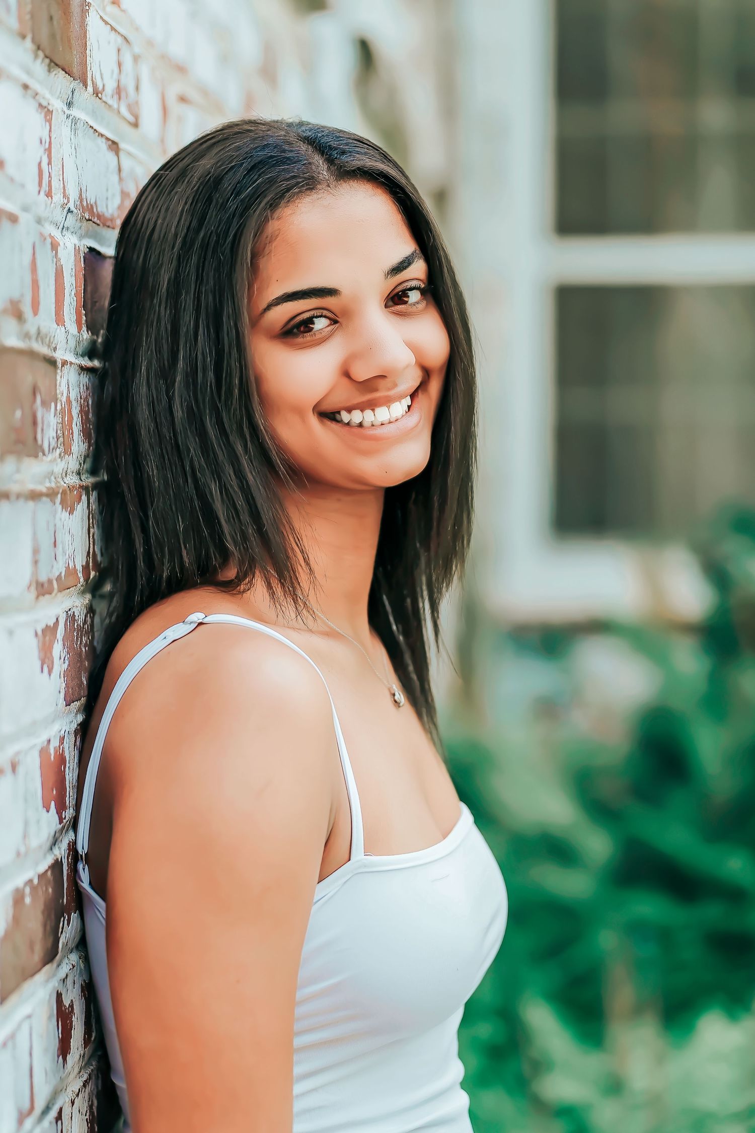 Portrait series against a brick wall with white tank top and natural lighting in an outdoor setting.
