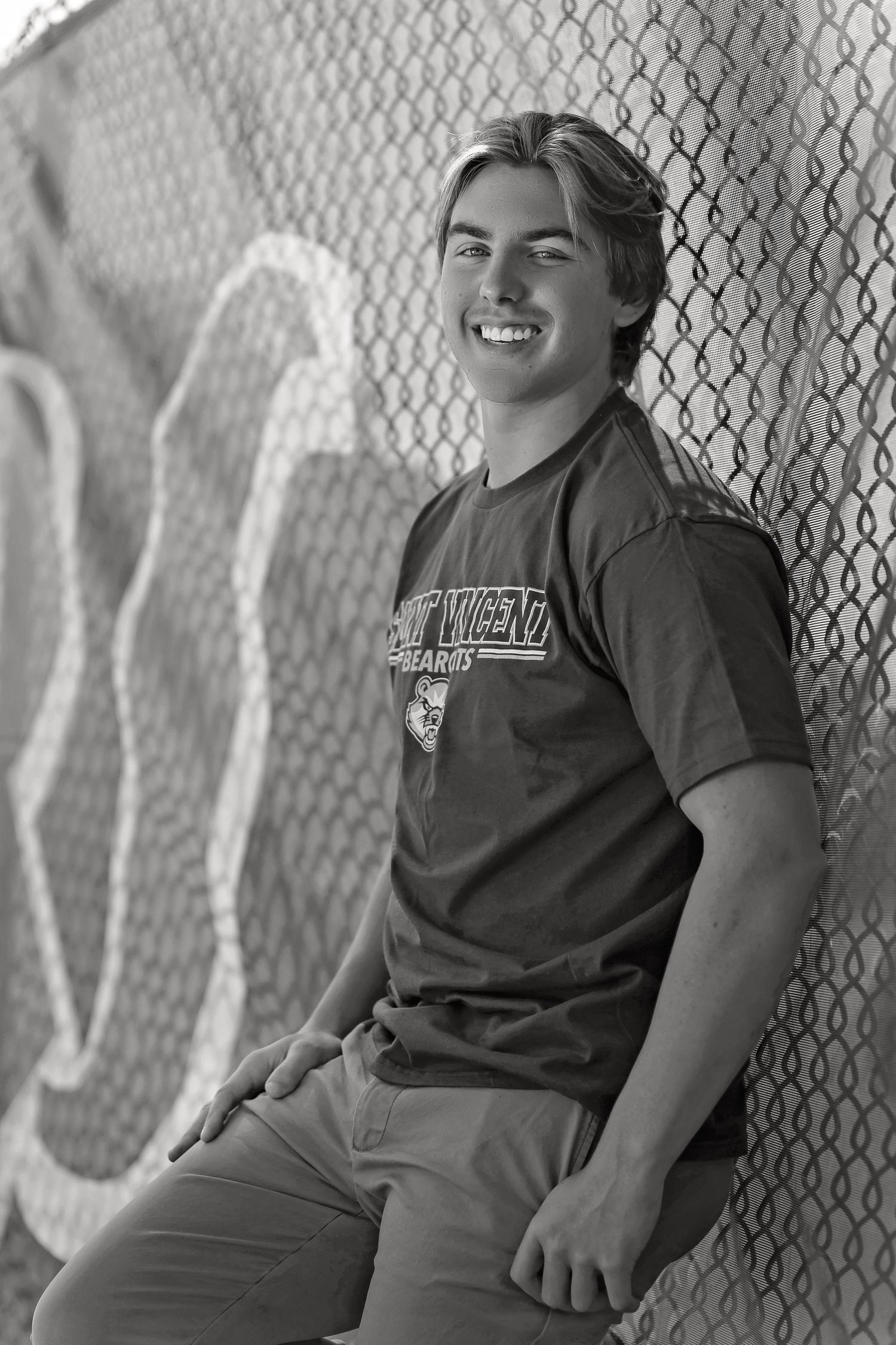 Black and white portrait series showing casual poses against a chain-link fence.