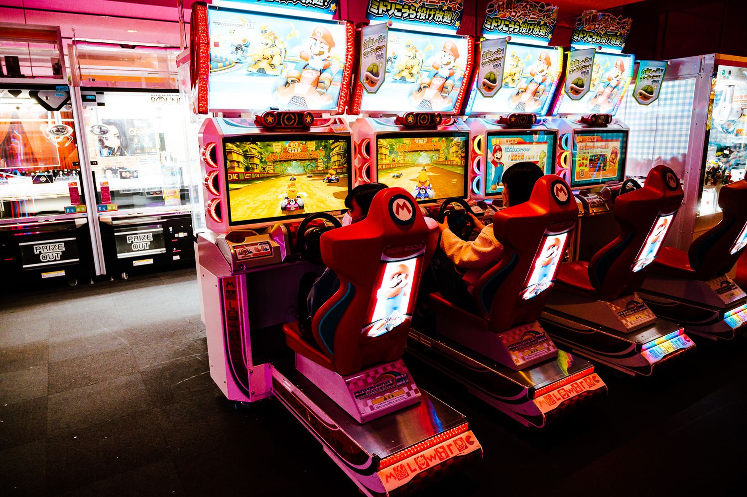 Colorful arcade racing games lined up in a dimly lit gaming center.