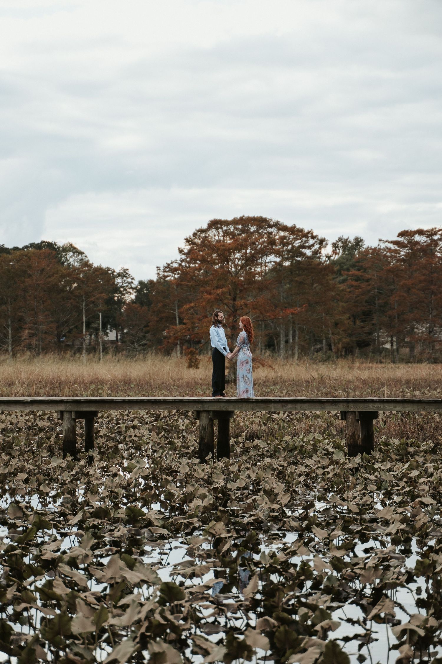 Couple in blue stands on a bridge in the distance with fall foliage in the background, for a small elopement.