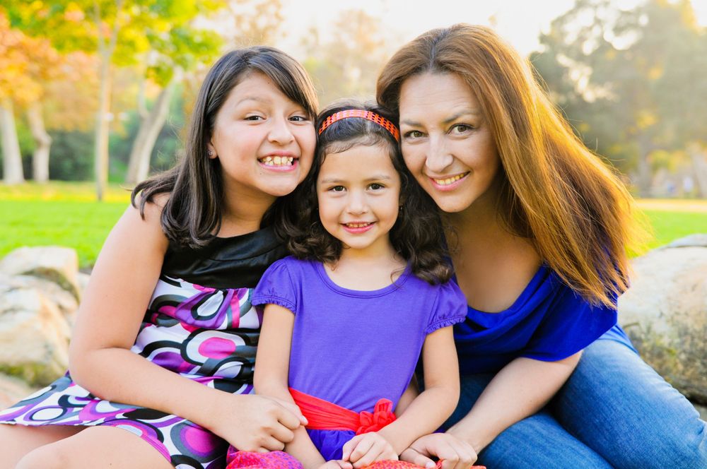 Three people sit together outdoors on sunny day with trees in background.