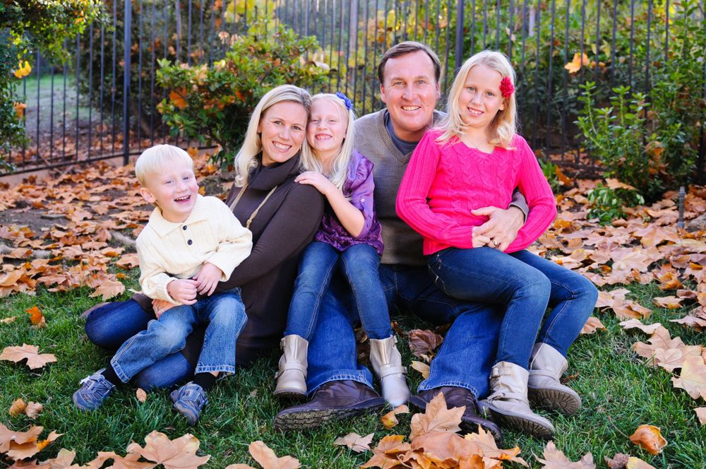 Family sitting together on grass surrounded by fallen autumn leaves.