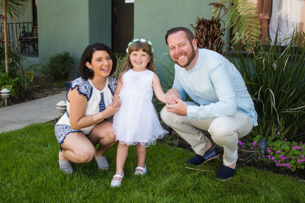 Family posing together on green lawn in front of house with tropical plants.