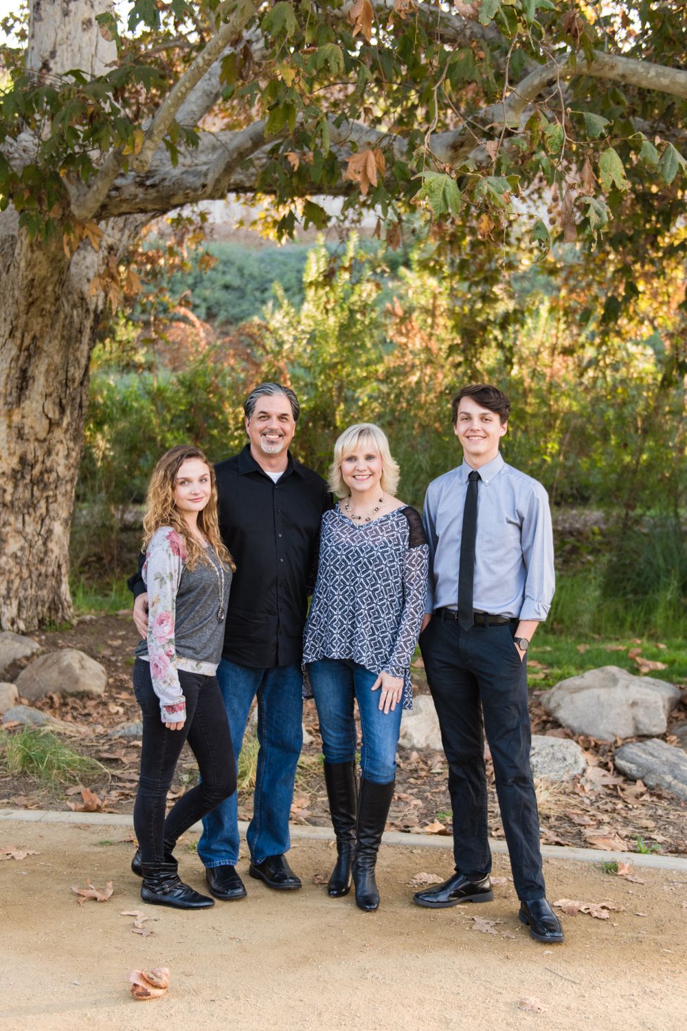 Family of four poses under large tree during sunset in casual attire.