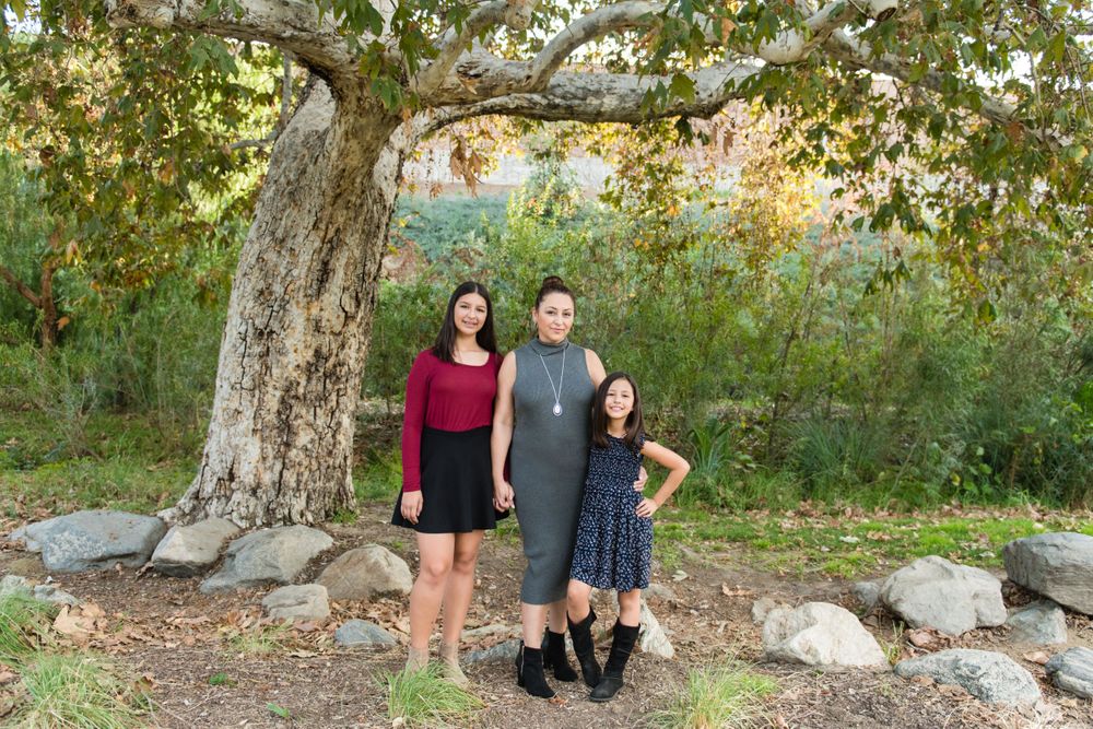 Three people standing under large tree with autumn foliage in natural outdoor setting.