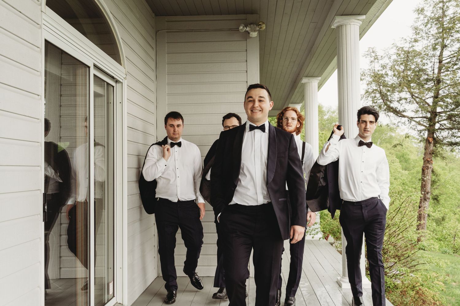 A group in formal attire poses on a white porch during a wedding celebration.