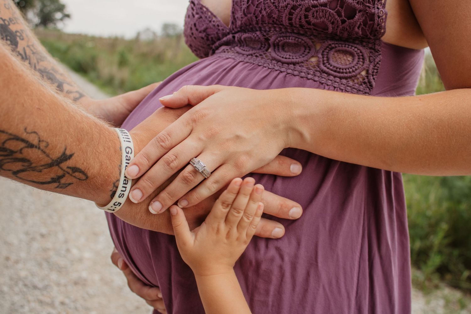 mother, infant, and husband resting their hands on pregnant belly