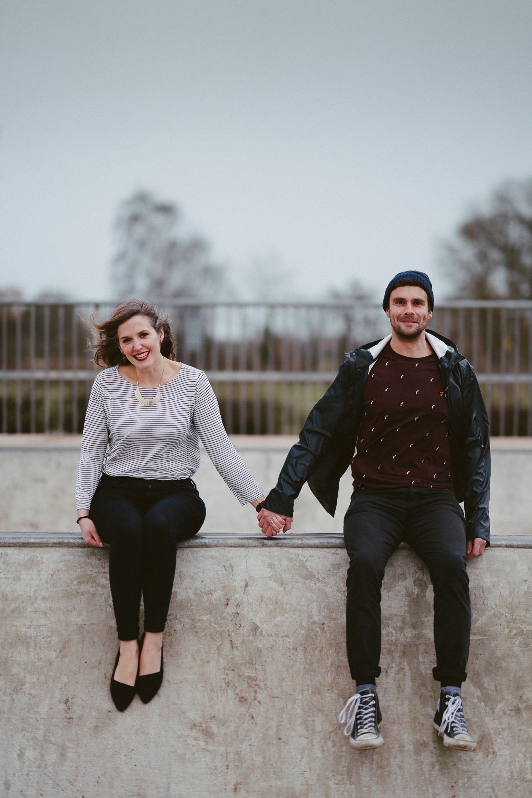 A couple sitting and laughing together on a concrete wall outdoors.