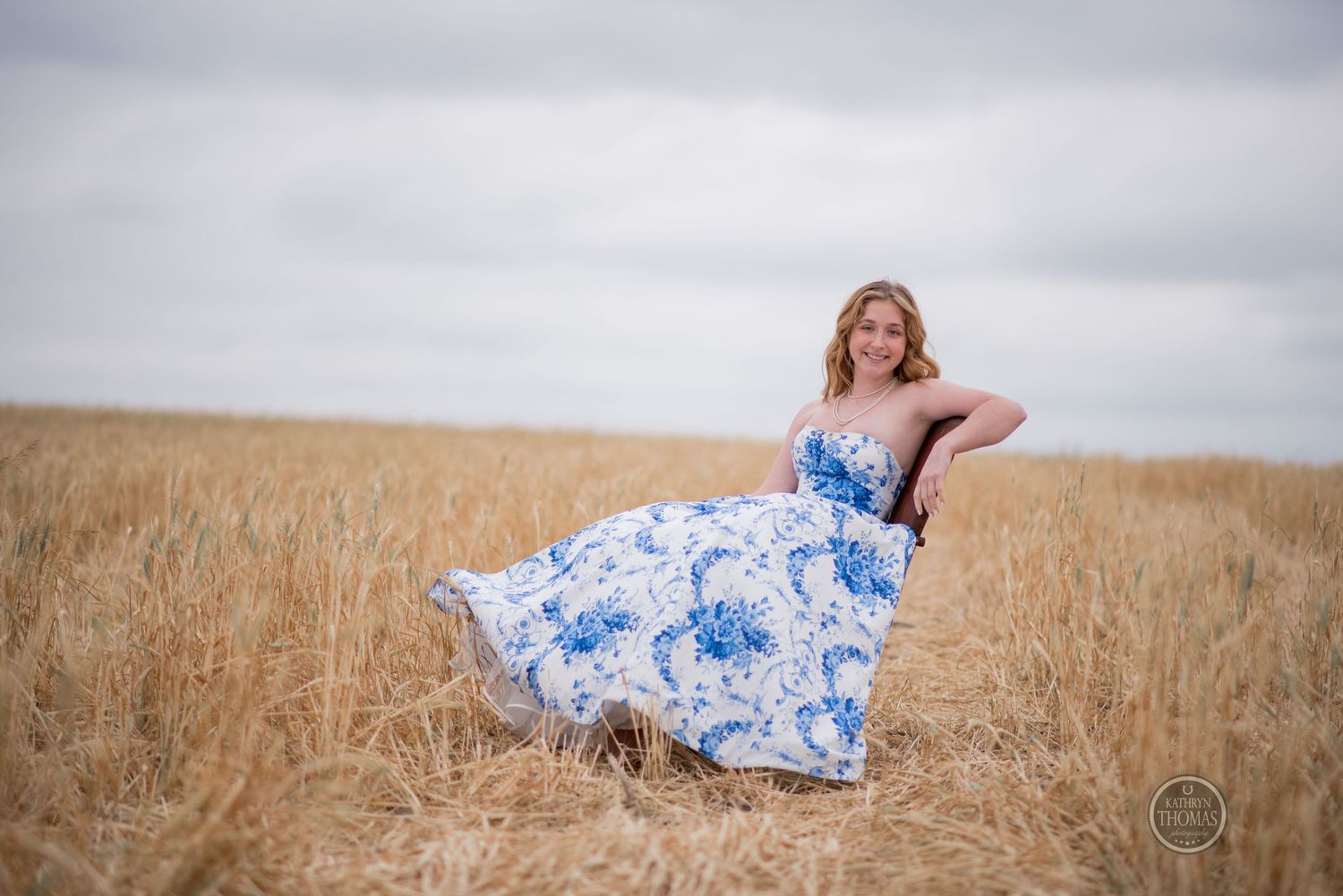Elegant pose in blue floral ballgown with wind-swept skirt in rustic field setting.