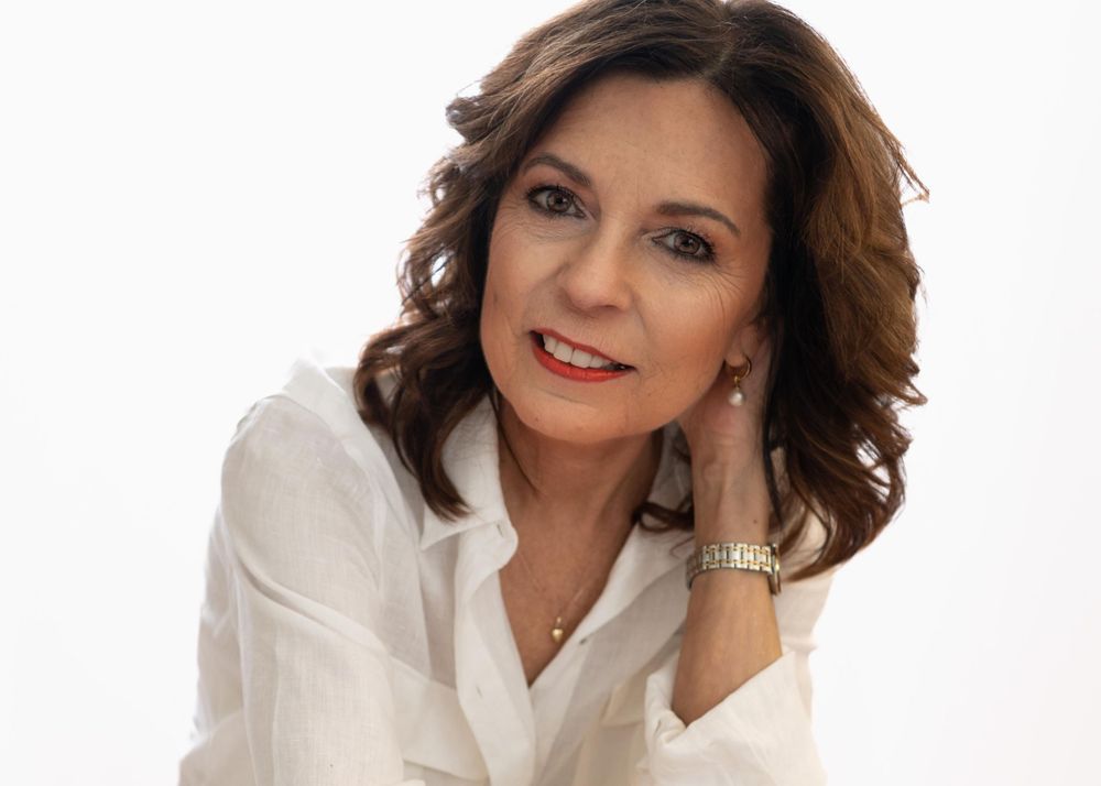 mooie vrouw van 60 plus in witte blouse en relaxte pose met een klein glimlachje