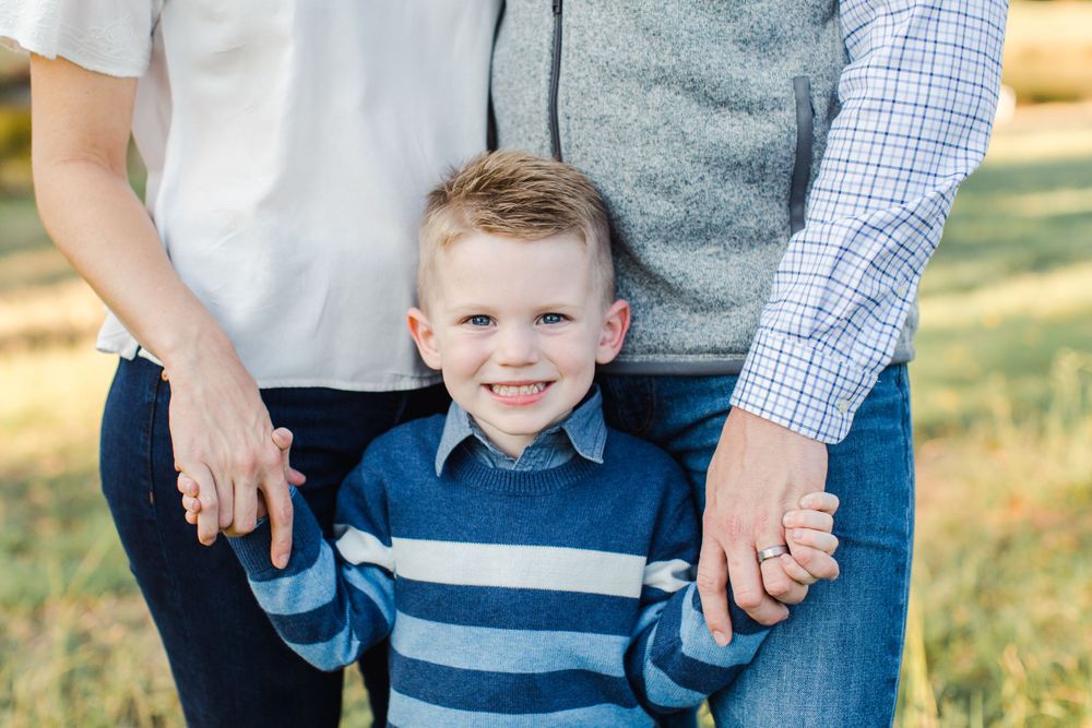 Close-up of young child holding parents' hands while wearing striped sweater.