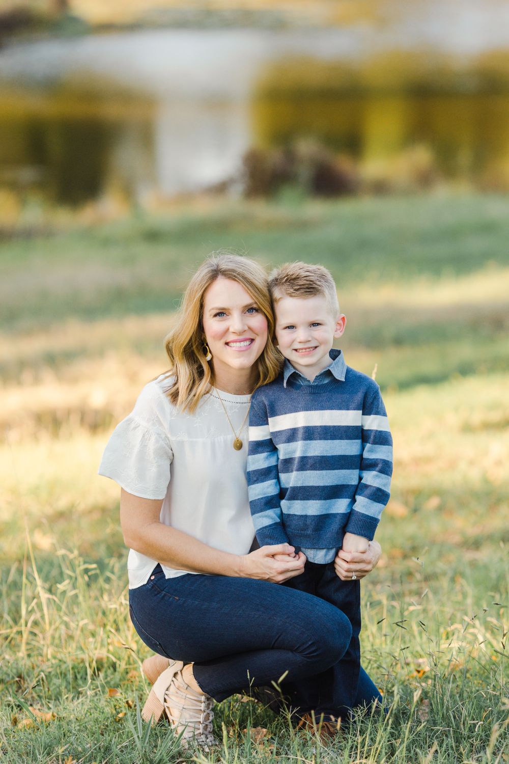 Mother and child in casual attire pose together in sunlit field.