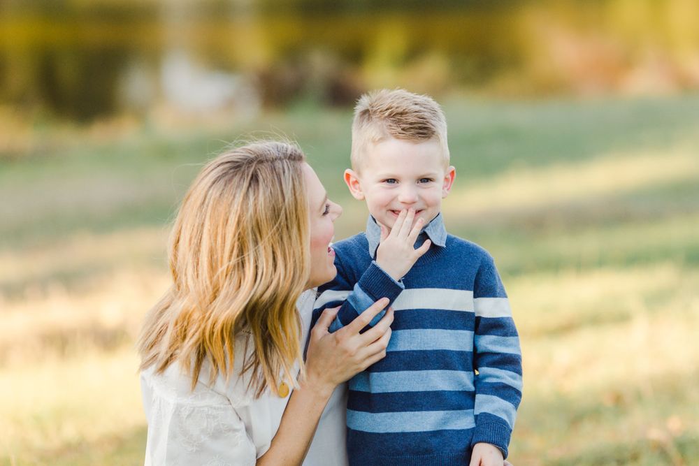 Parent and child share a laugh while looking at a mobile phone in an outdoor setting.