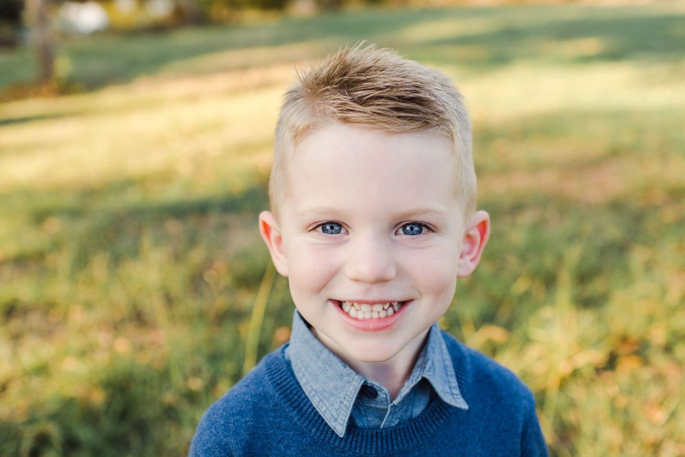 Portrait of a young child wearing a blue sweater smiling brightly at the camera.