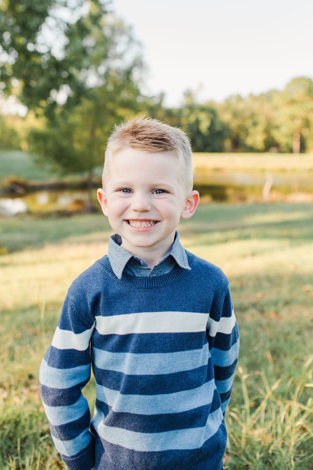 Cheerful portrait of a child in a blue striped sweater against a natural backdrop.