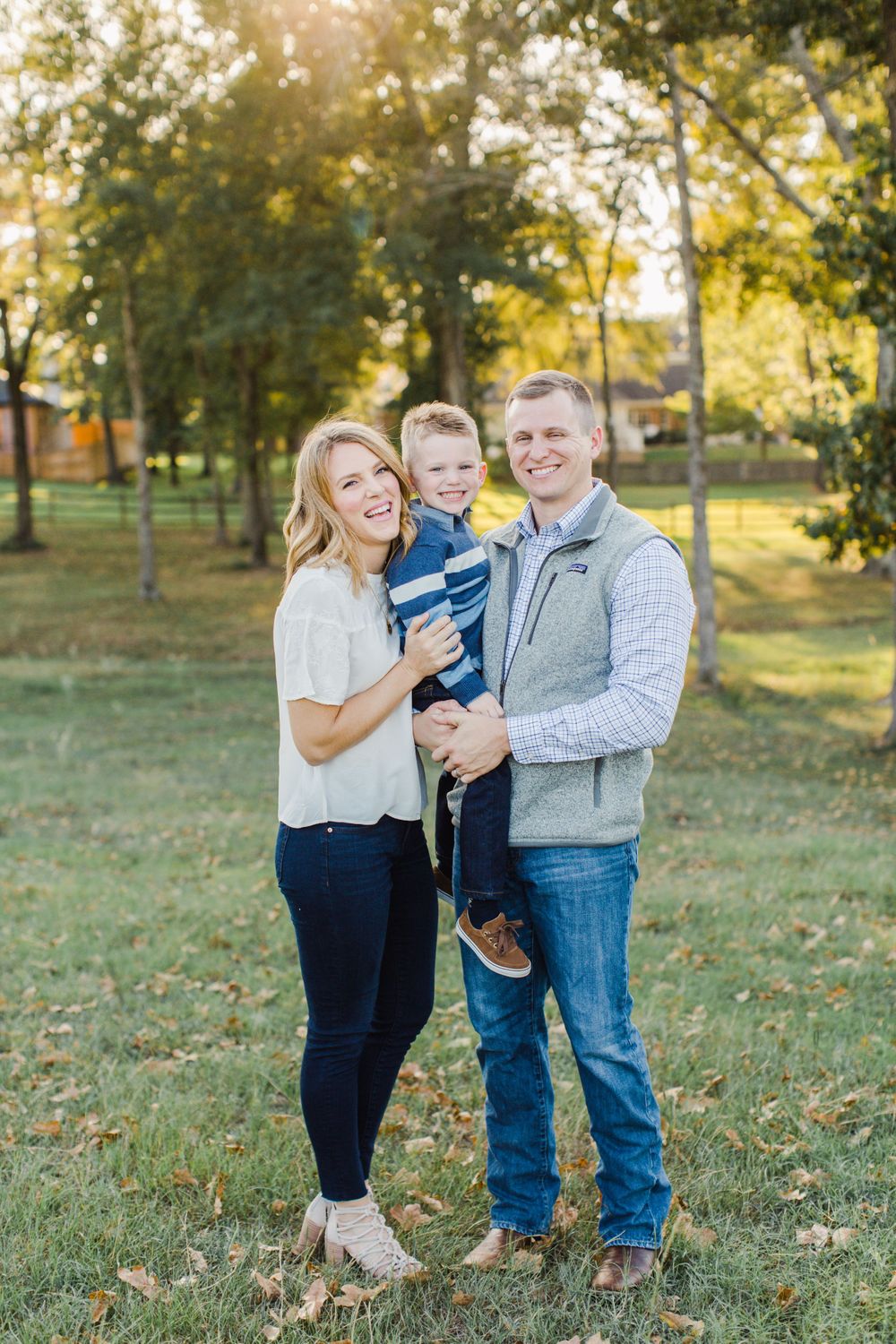 A family portrait captured in a park during golden hour with trees in the background.